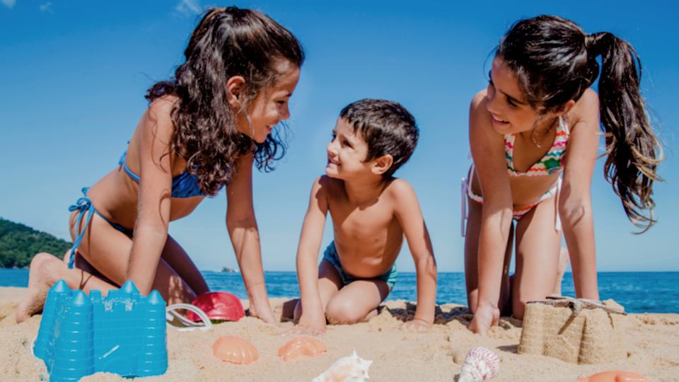 Дети на пляже. Две девочки и мальчик играют на песке. Маленькие девочки на пляже.